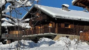 Uma cabana de madeira com telhado coberto de neve e uma varanda, rodeada por neve.