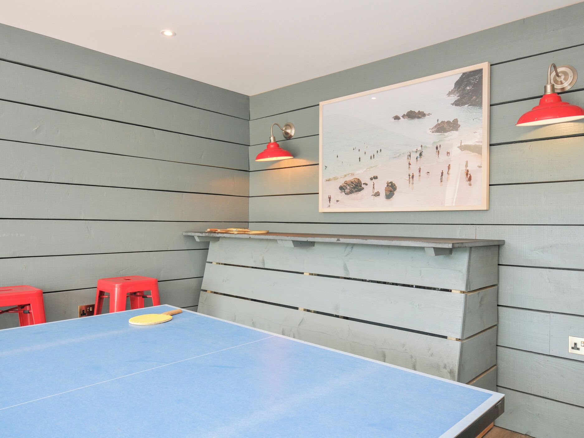 Una mesa de ping pong con taburetes rojos, una chimenea y un cuadro en la pared.