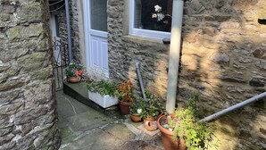 A stone building with a white door and window, potted plants on the steps, and a stone wall. - Bracken Cottage (Bishop Auckland)