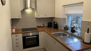 A compact kitchen with white cabinets, a stainless steel sink, and a window with a view of the outdoors. - Bracken Cottage (Bishop Auckland)