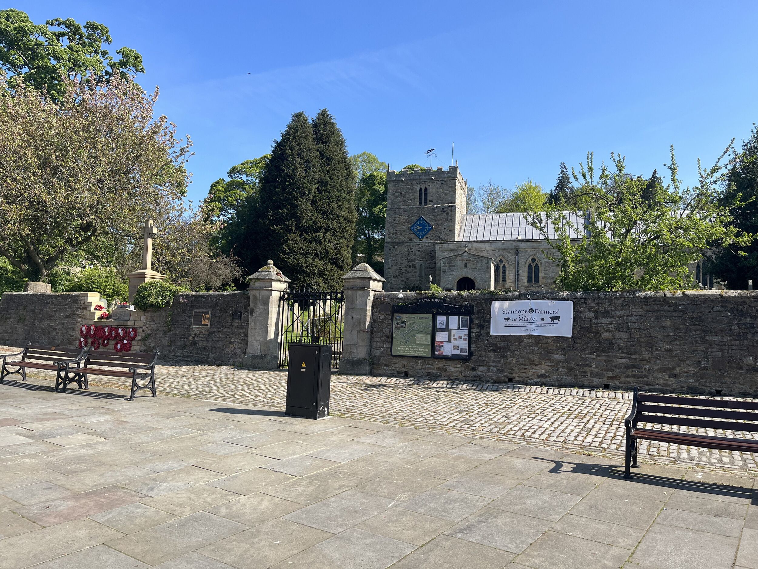 A stone wall with a gate, a bench, and a sign for Stanhope Farmers' Market.
