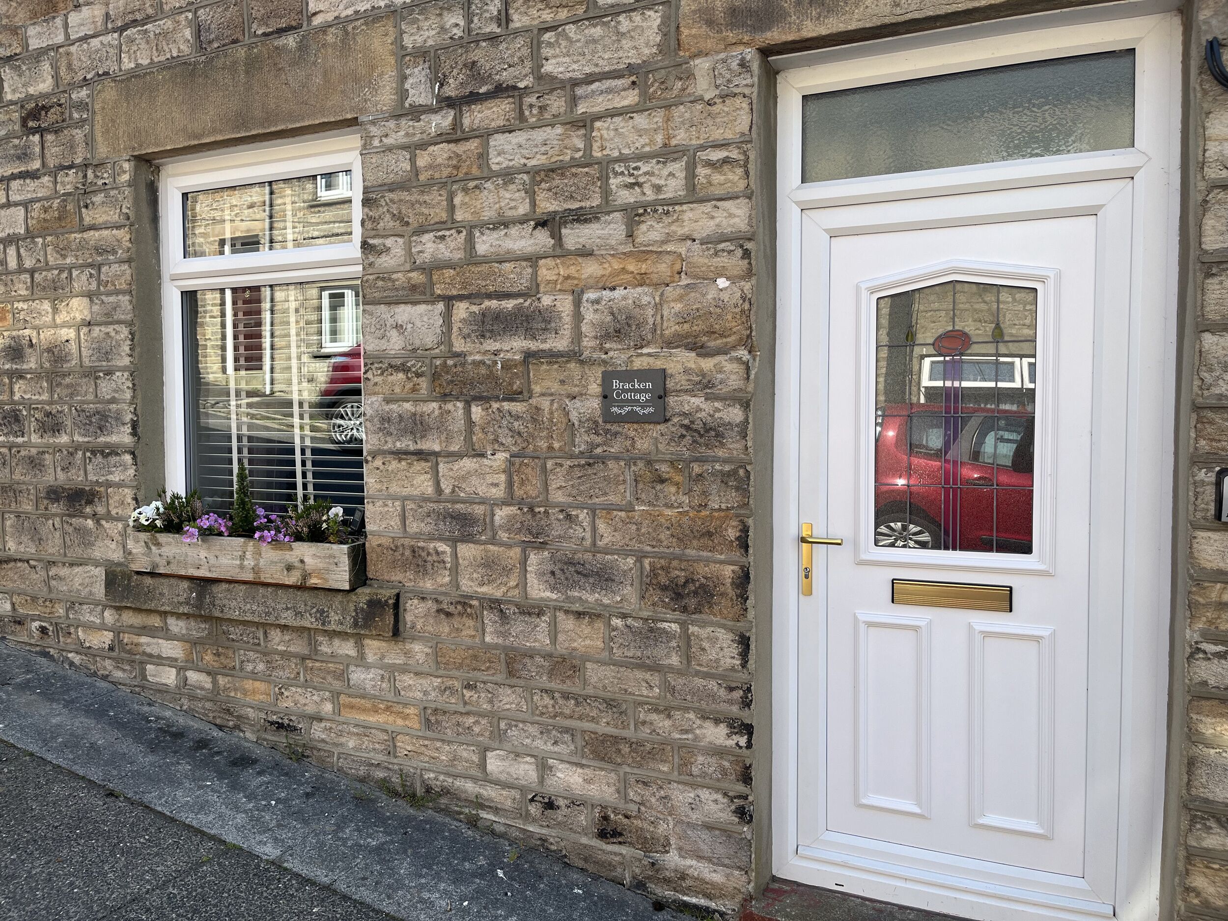 A stone building with a white door and a window with a sign reading "Bracken Cottage."