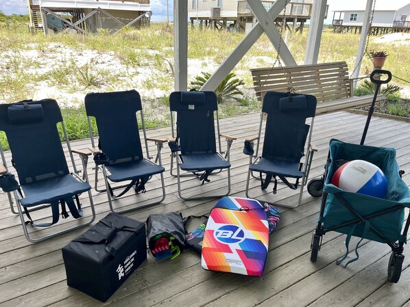 A wooden deck with four blue folding chairs, a bench, and a beach ball in a teal bag.