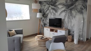 Un saló modern amb televisió de pantalla plana, sofàs grisos, un moble blanc i paper pintat amb motius de fulles tropicals.