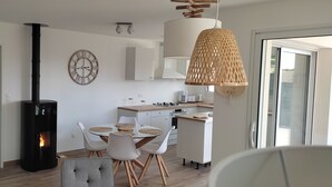 Una cuina moderna amb una illa central, una zona de menjador amb taula rodona i cadiretes, un rellotge gran a la paret i una llar de foc.