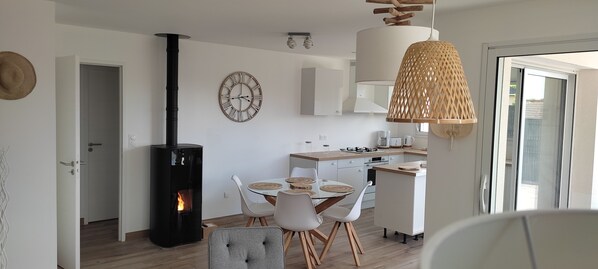 A modern kitchen with a central island, a dining area with a round table and chairs, a large clock on the wall, and a fireplace.