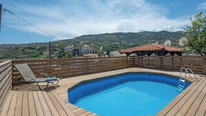 Een houten terras met een zwembad, een overdekte zithoek en uitzicht op een glooiend landschap.