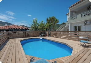 Une terrasse en bois avec une piscine, un banc en bois et une petite table.