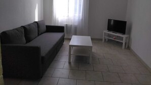 A living room with a grey sofa, a white coffee table, a TV on a stand, and a window with sheer curtains. - Pretty Apartment 15 min walk from the Promenade des Anglais (Nice)