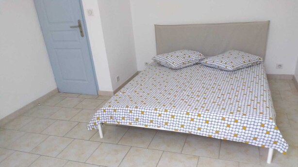 A single bed with a patterned bedspread and two pillows, a light blue door, and a tiled floor. - Pretty Apartment 15 min walk from the Promenade des Anglais (Nice)