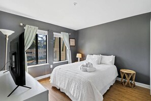 A bedroom with a bed, a desk, a lamp, and a window with curtains.