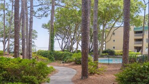 A pathway leading to a pool surrounded by tall trees and a building with balconies. - Port Royal Sound 2BR Villa Balcony, Pools & Beach Access (Hilton Head Island)