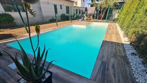 Uma piscina retangular com água azul cristalina, ladeada por um deck de madeira e uma borda de pedra baixa.