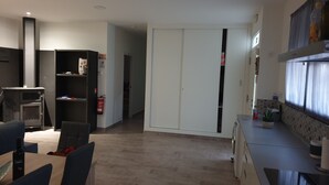 Uma cozinha moderna com forno embutido, área de refeições com mesa e cadeiras, e um guarda-roupa com portas de correr.