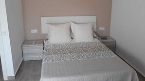 Quarto com cama, duas almofadas, mesa de cabeceira e um móvel com gavetas.
