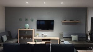 Uma sala de estar moderna com uma TV de tela plana fixada na parede, um armário de madeira, um sofá e uma mesa de centro.