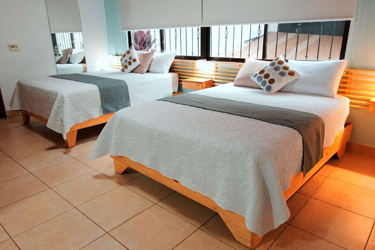 Two single beds with wooden frames and white bedding, a window with blinds, and a tiled floor.