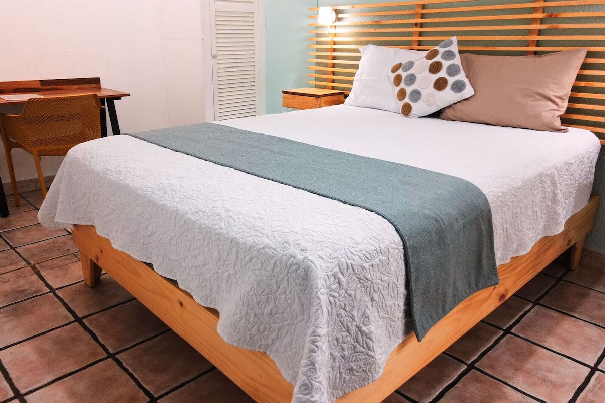 A bed with a white and teal bedspread, a wooden headboard, and two pillows with a polka dot design.