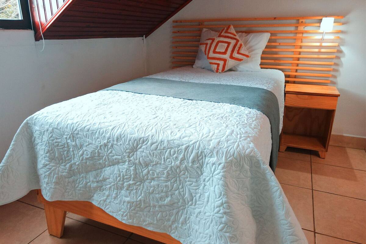A bedroom with a bed, wooden headboard, nightstand, and a window with blinds.