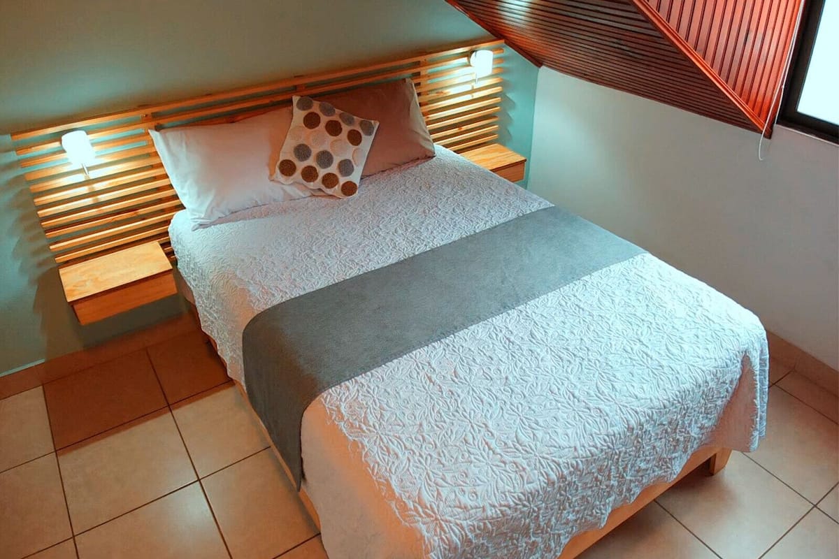 A neatly made bed with a patterned pillow, a grey blanket, and wooden headboards.