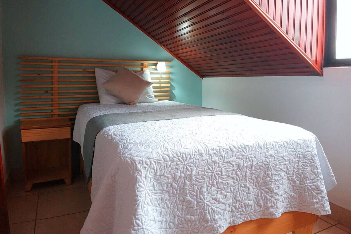 A bedroom with a wooden slat headboard, a bed with a white quilt, and a small wooden nightstand.