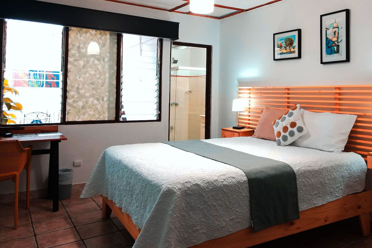A bedroom with a bed, bedside tables, a desk, and a chair. There are two framed pictures on the wall.