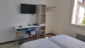 A bedroom with a bed, a desk, a chair, a TV, and a wardrobe.