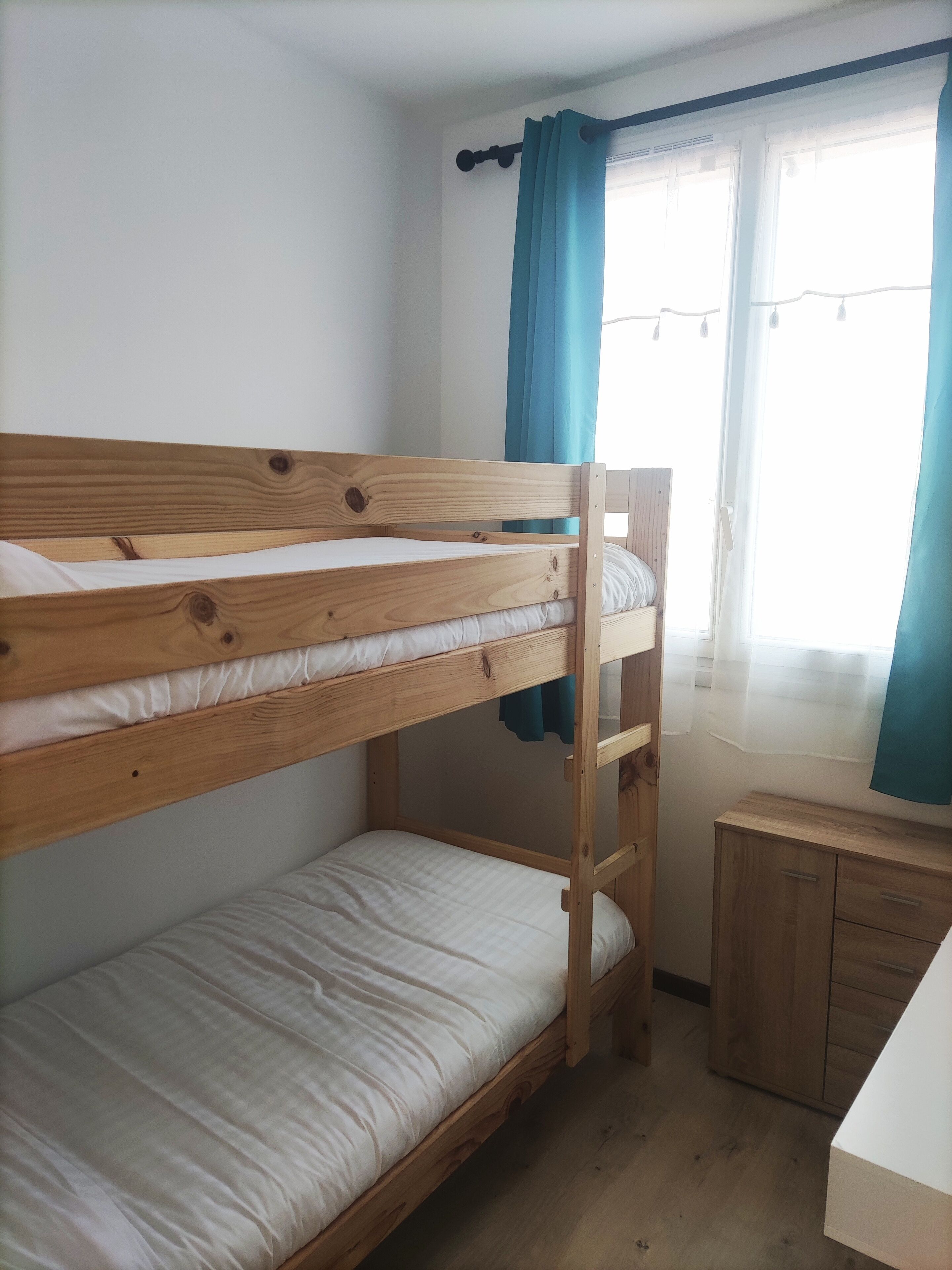 Ein Schlafraum mit Etagenbetten, einem hölzernen Kopfteil, einem kleinen Schreibtisch und einem Fenster mit Vorhängen.