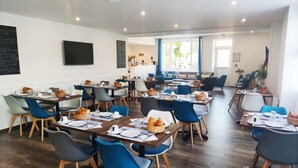 Een moderne eetruimte met meerdere tafels en stoelen, een bord met krijtmenu en uitzicht op de omgeving.
