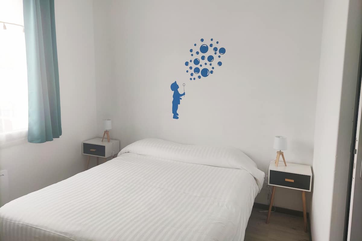 Een slaapkamer met een bed, twee nachtkastjes, een muursticker en een raam met gordijnen.