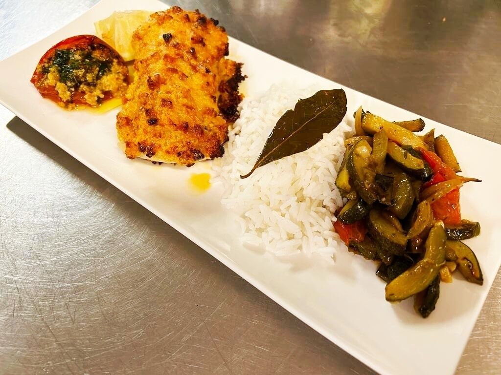 A rectangular plate with white rice, a piece of fried chicken, a vegetable stir-fry, and a small portion of what appears to be a tomato-based dish.