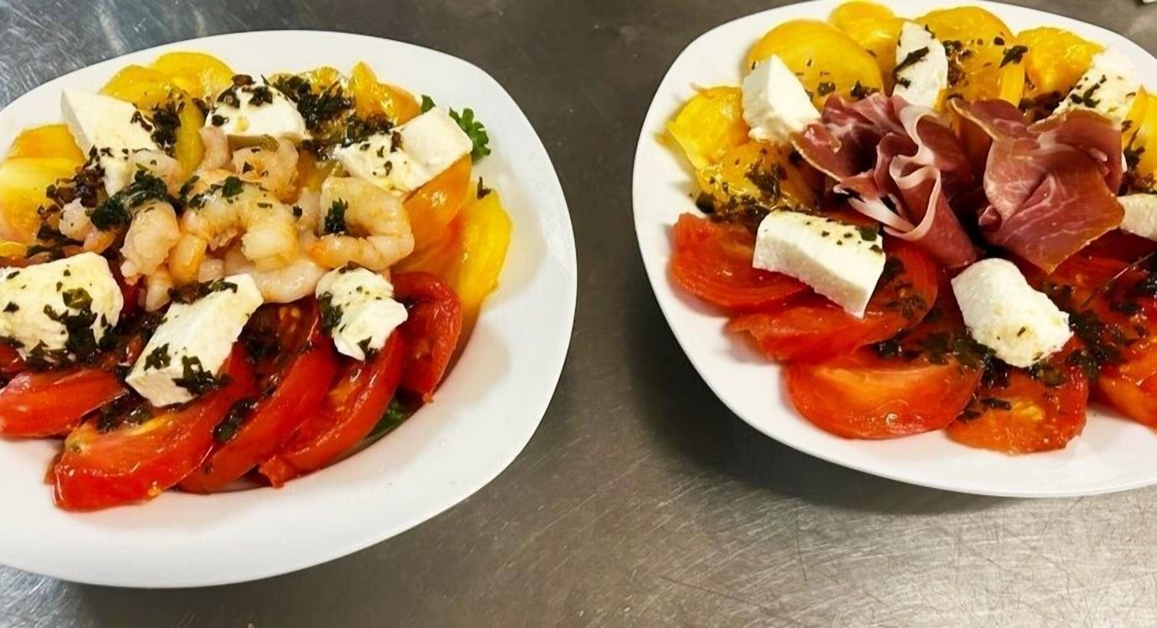 Two plates of food with tomatoes, cheese, and herbs.
