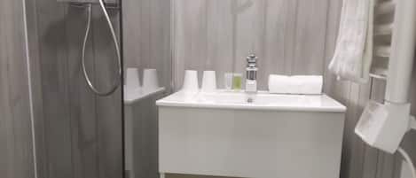 Un baño con ducha, lavamanos y artículos de aseo, y un espejo.