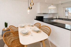 Une cuisine moderne avec des meubles blancs, un plan de travail noir et un coin repas doté d’une table blanche, mise pour six personnes.