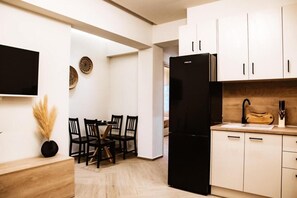 A modern kitchen with white cabinets, a black refrigerator, and a dining area with a table and chairs.