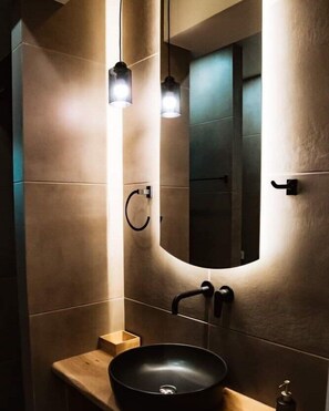 A modern bathroom with a large mirror, a black sink, and pendant lighting.