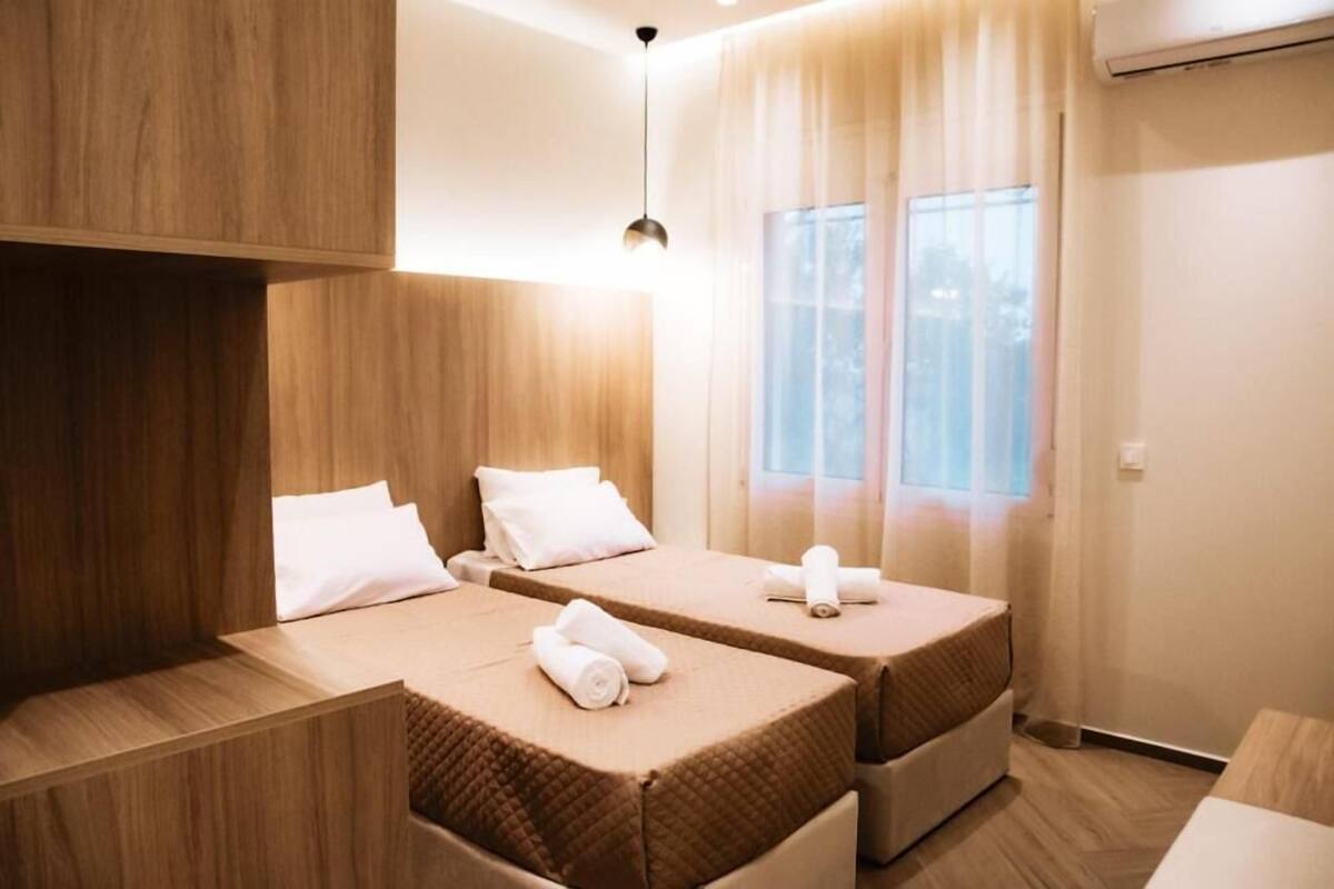 A hotel room with two beds, wooden paneling, a large window with curtains, and a hanging light fixture.