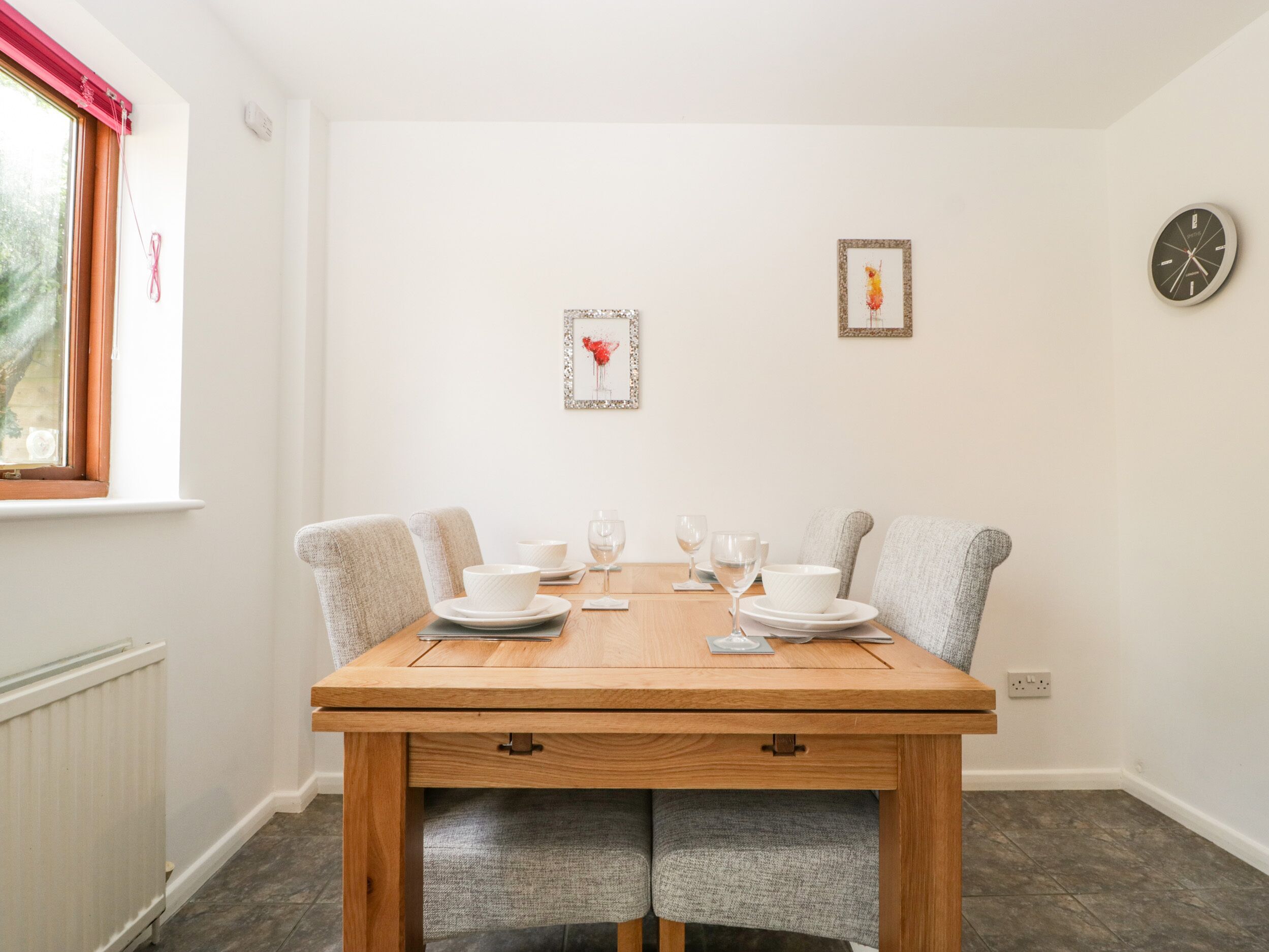 Un coin repas avec une table en bois, deux chaises grises à revêtement rembourré, des assiettes blanches et des verres à vin.