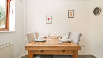 Un coin repas avec une table en bois, deux chaises grises à revêtement rembourré, des assiettes blanches et des verres à vin.