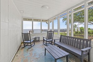 A covered outdoor seating area with a bench and chairs, overlooking a body of water and a pier. - Bayfront Property - Sunsets, Fishing, Wildlife Viewing (Gulf Shores)
