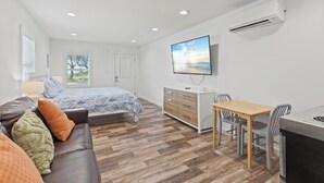Ein Schlafzimmer mit einem Bett, einem Schminktisch, einem Fernseher, einem Schreibtisch mit Stühlen und einer Klimaanlage.