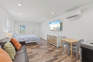 Une chambre à coucher comprenant un lit, une commode, un téléviseur, un bureau avec des chaises et un appareil de climatisation.