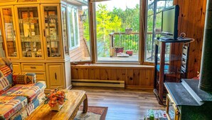 A cozy living room with a wooden bench, a colorful sofa, a wooden coffee table, and a television on a stand. - Gorgeous 3 bed rooms waterfront cottage on Kennebec Lake (Arden)