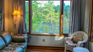 A cozy room with a large window, a ceiling fan, a leather sofa, a wicker chair, and a patterned rug. - Gorgeous 3 bed rooms waterfront cottage on Kennebec Lake (Arden)