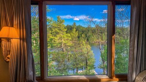 A room with a large window offering a view of a lake surrounded by trees. - Gorgeous 3 bed rooms waterfront cottage on Kennebec Lake (Arden)