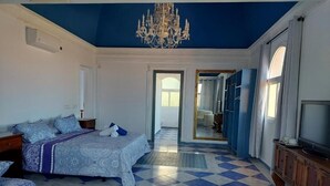 A bedroom with a checkered floor, a bed with a patterned bedspread, a chandelier, and a television on a wooden cabinet. - Villa Zafira (Benalmádena)