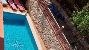 A swimming pool with a stone wall and a tiled deck area. - Villa Zafira (Benalmádena)
