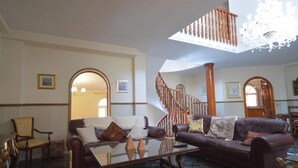 A spacious living room with a high ceiling, a chandelier, a staircase, and a large window. - Villa Zafira (Benalmádena)