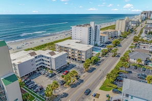 A coastal hotel with multiple floors, a parking lot, and a beach view.