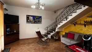 A living room with a flat-screen TV, a rocking chair, a sofa, a coffee table, and a staircase with a decorative railing.